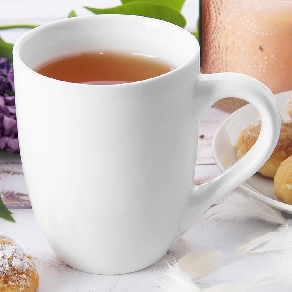 Una taza blanca de té sobre mesa con galletas, flores y plumas.