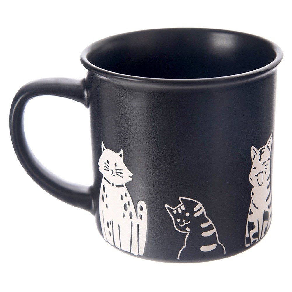 Taza negra con diseños de gatos blancos. Se representan tres gatos.