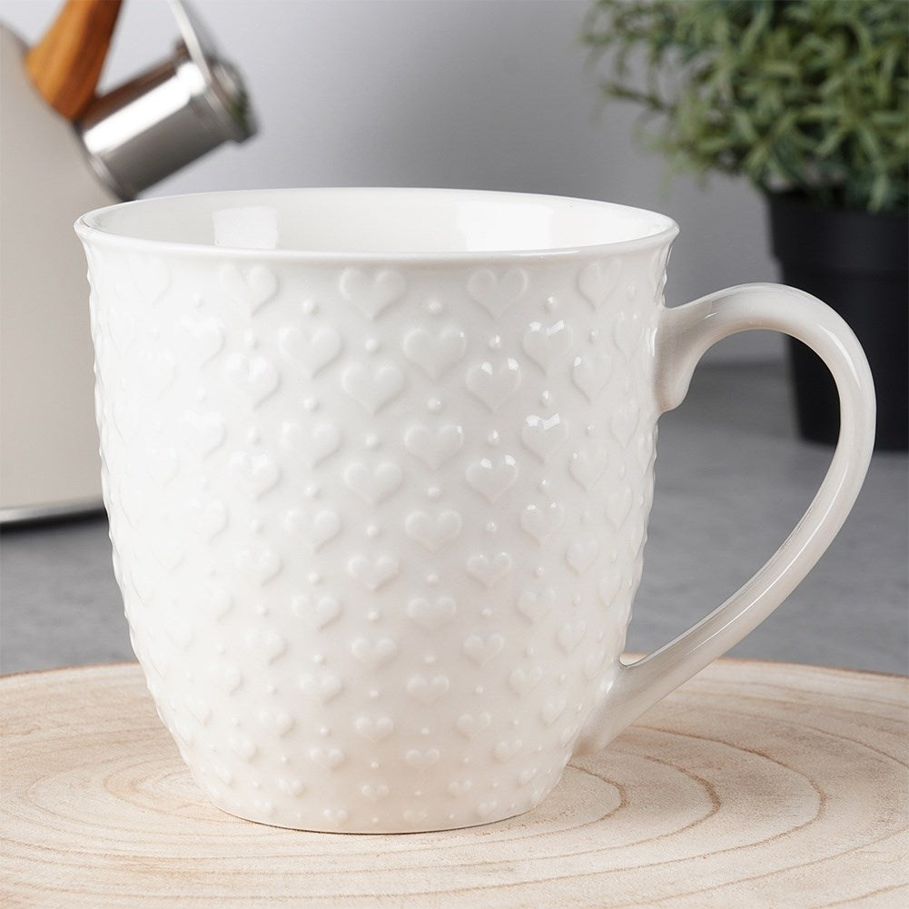 Taza blanca con patrón de corazón en relieve sobre madera.