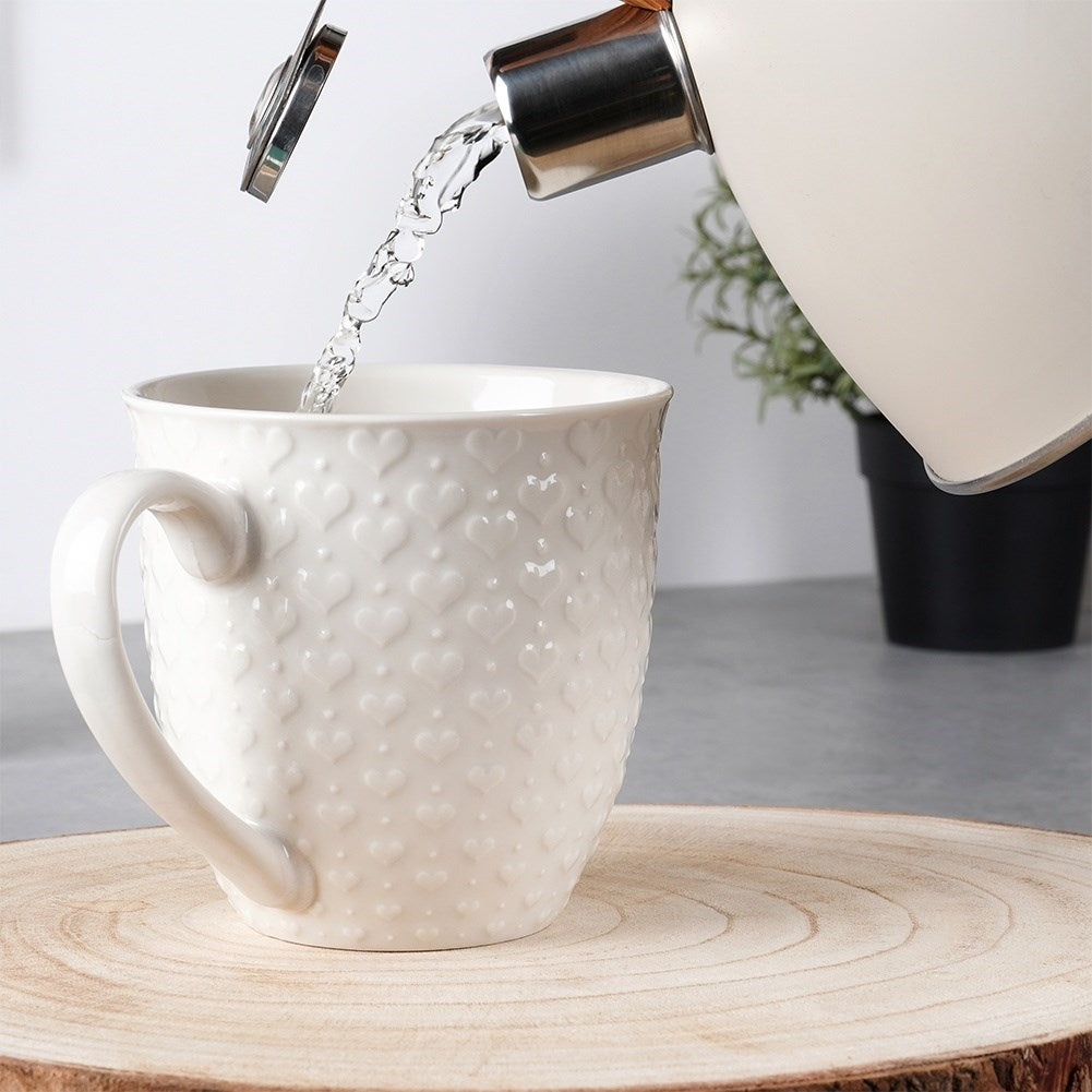 Se vierte agua de una tetera en una taza blanca con diseño de corazones.