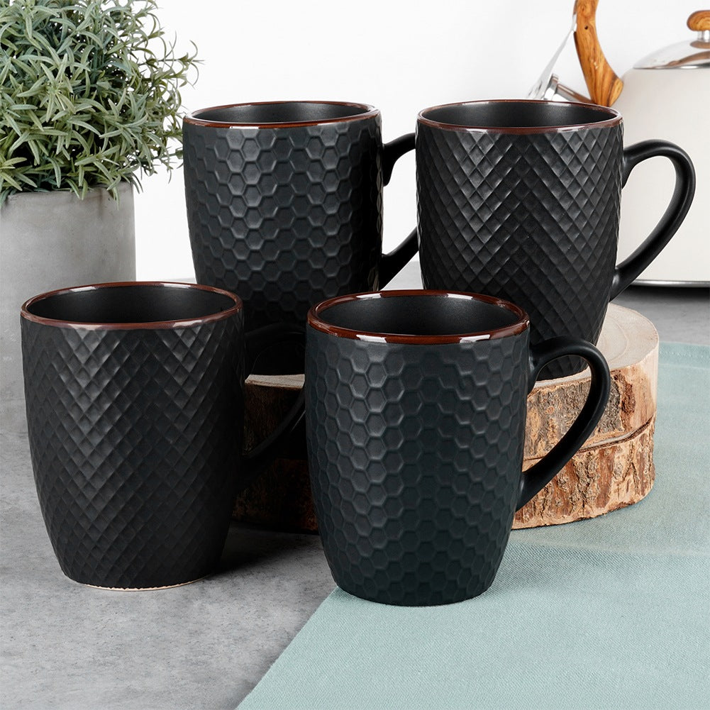 Cuatro tazas negras con patrones de panal y diamantes sobre una mesa.