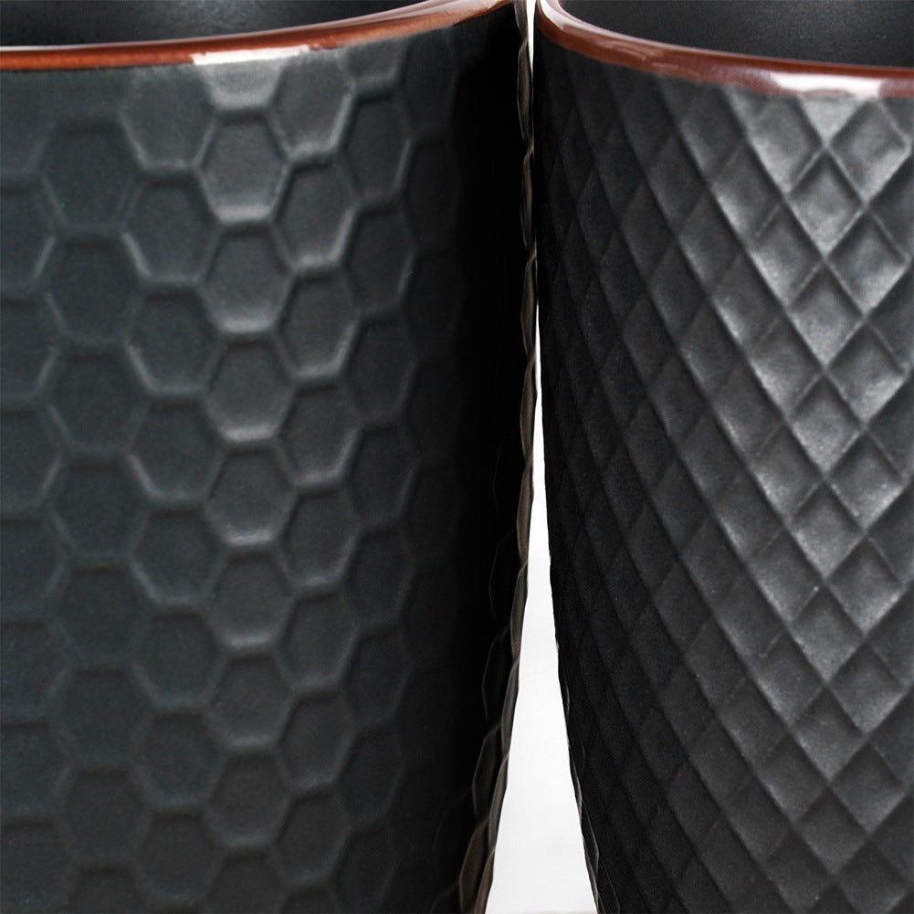 Dos tazas negras con texturas diferentes. Una tiene un patrón de panal, la otra un patrón de diamantes.
