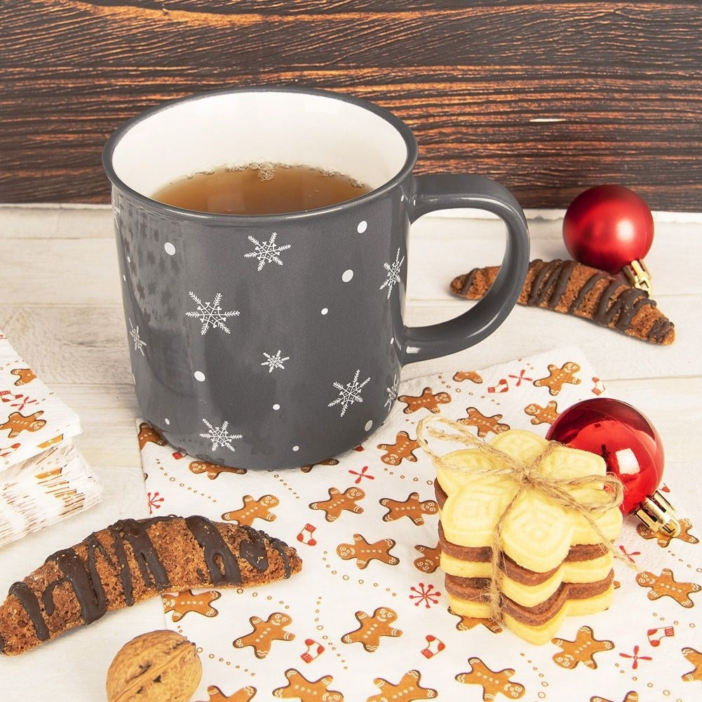 Taza gris con copos de nieve, galletas, decoración navideña y bebida.