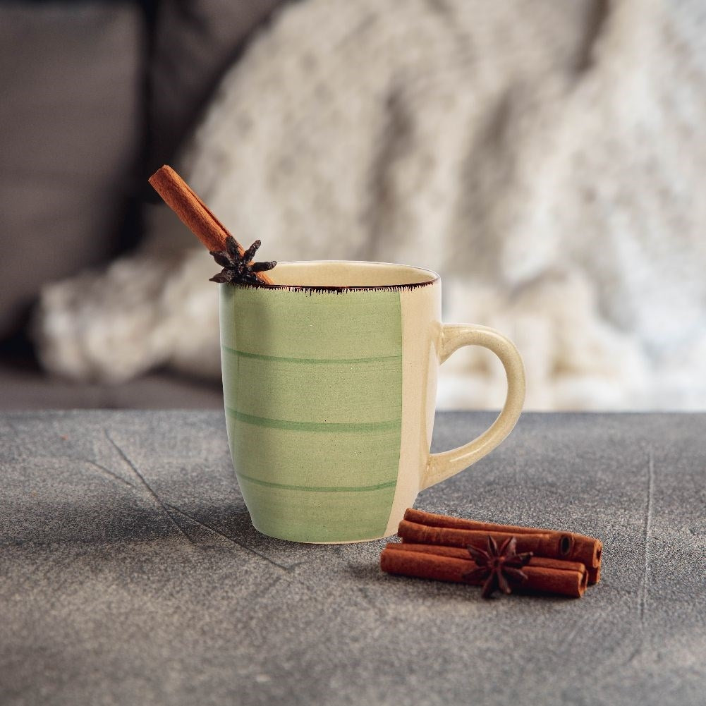 Una taza verde y crema con canela y anís estrellado sobre una superficie texturizada.