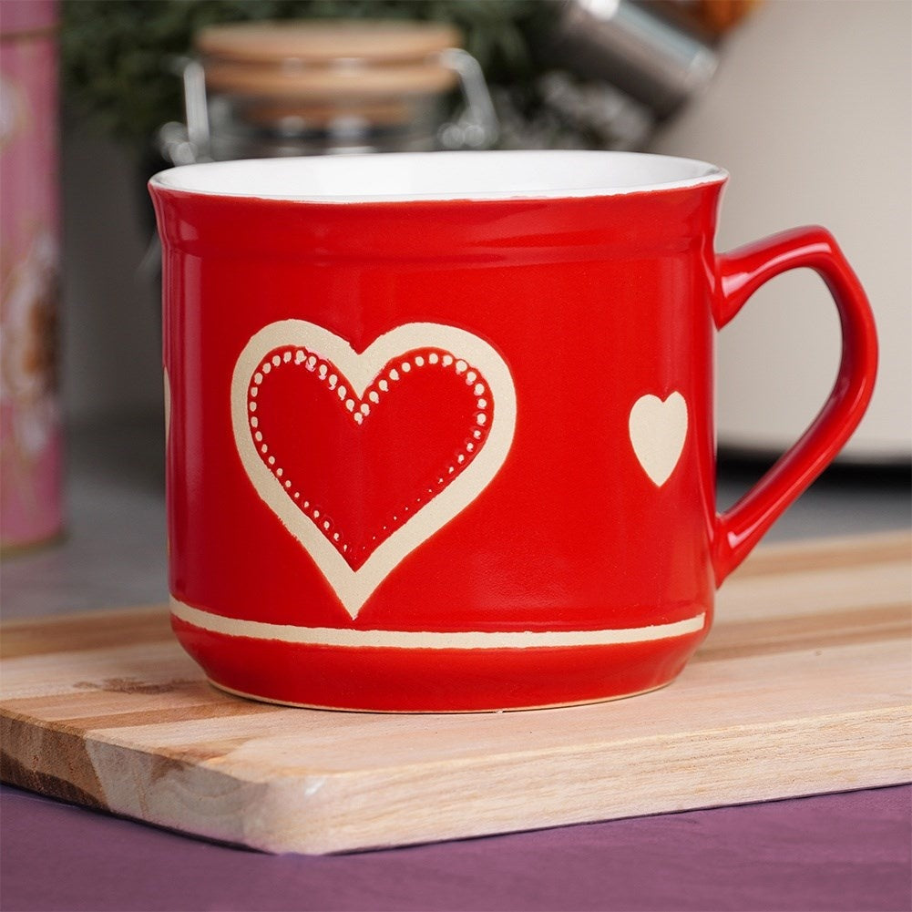 Taza roja con diseño de corazón, borde blanco, sobre tabla de madera.