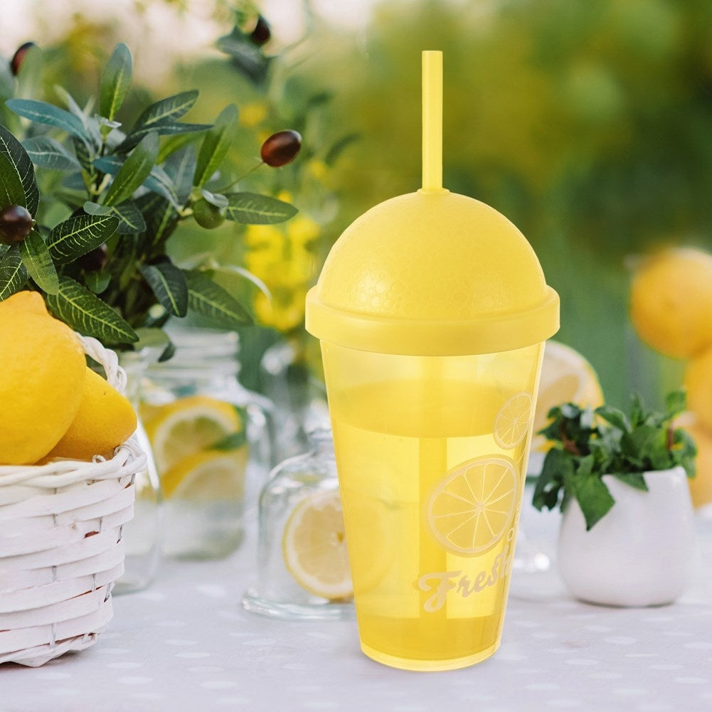 Un vaso amarillo con pajita sobre una mesa con limones y hojas.