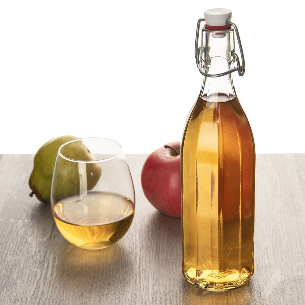Una botella de líquido ámbar junto a un vaso del mismo líquido, con una manzana y una pera.