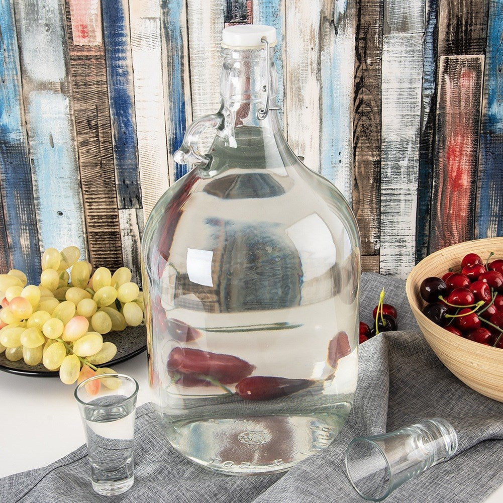 Botella grande de vidrio con tapa abatible, llena de líquido transparente, junto a uvas y cerezas.