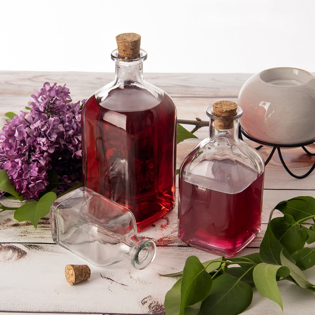Tres botellas de vidrio con corcho, dos llenas de líquido rojo, una vacía.