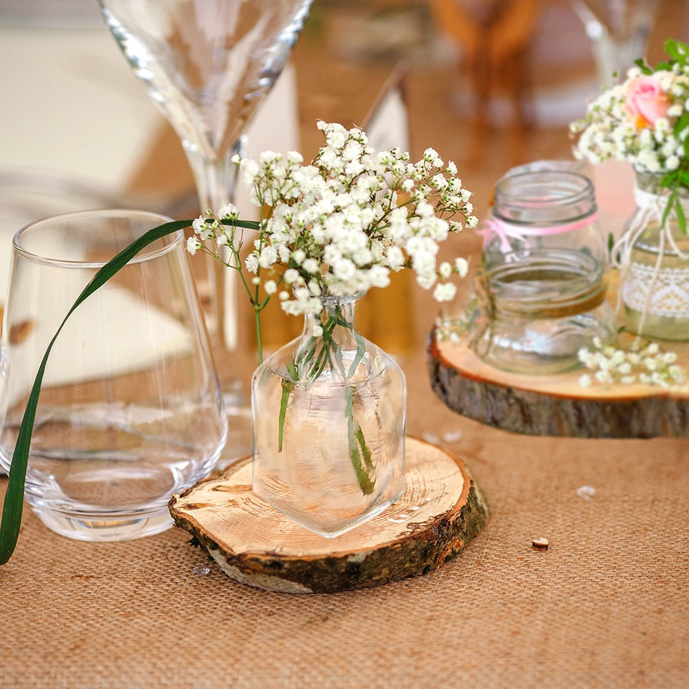 Decoración de mesa con flores en jarrones de vidrio sobre rodajas de madera en yute.