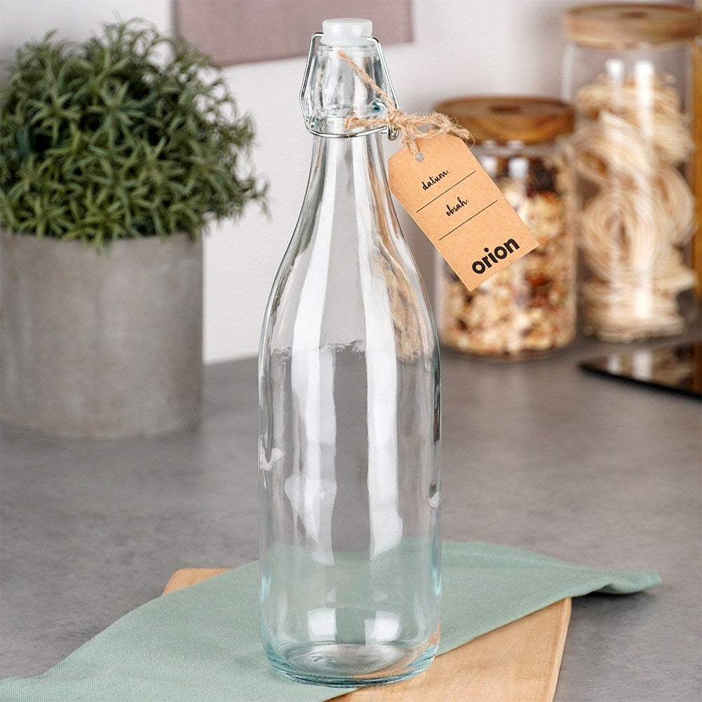 Una botella de vidrio transparente con cierre abatible y etiqueta marrón está sobre una mesa.
