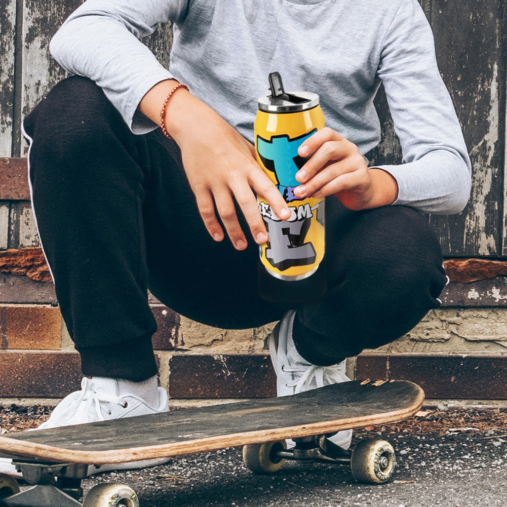 Persona con camiseta gris, pantalones negros, zapatos blancos sostiene lata amarilla. Patineta delante.
