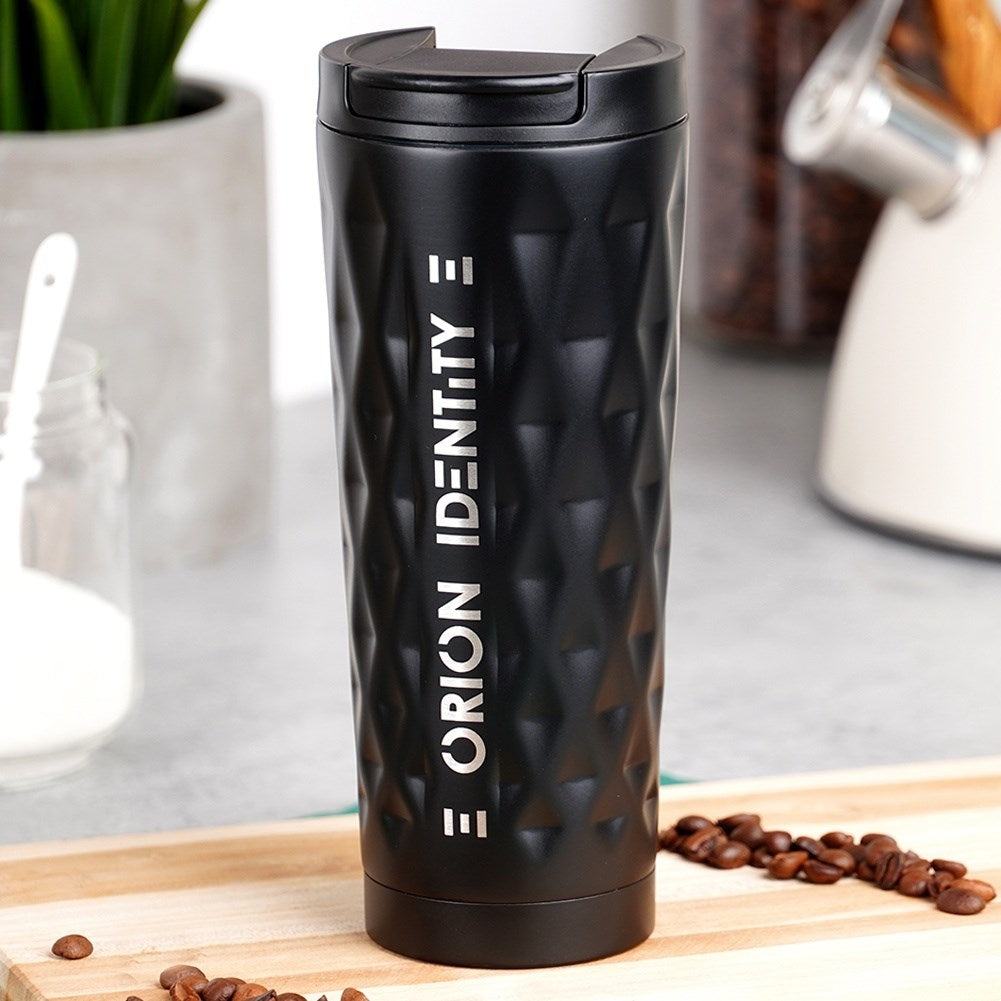 Vaso negro con patrón de diamantes y texto, junto a granos de café.