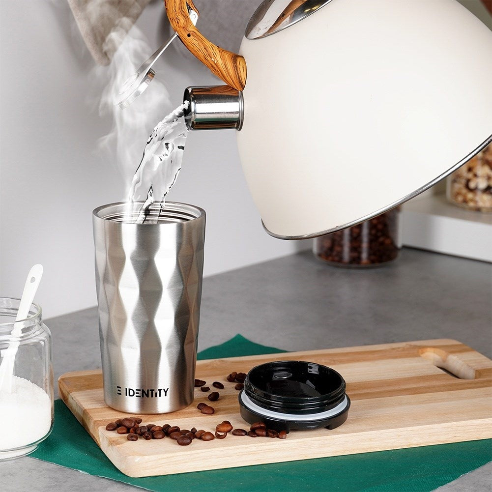 Se vierte agua caliente de una tetera en un vaso plateado, con granos de café cerca.