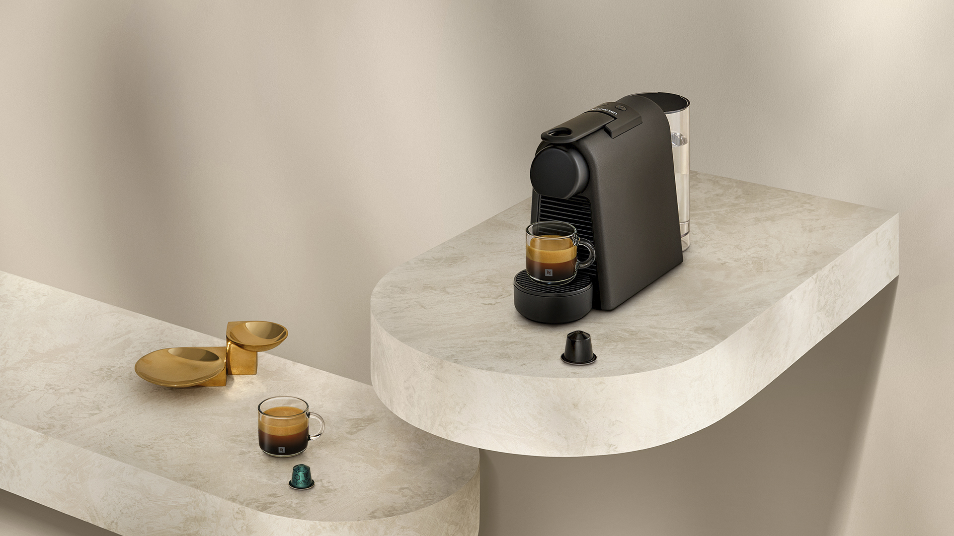 Una macchina da caffè nera con tazza di espresso, capsule e un piatto dorato.