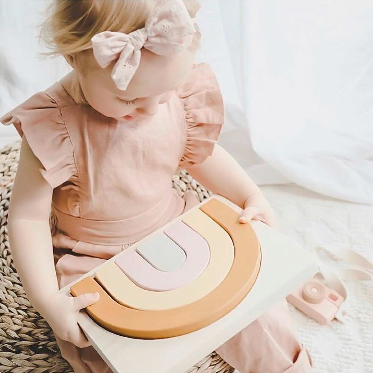Una niña con un atuendo rosa juega con un rompecabezas de arcoíris de madera.