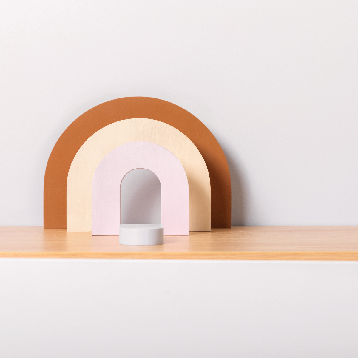 Un arcoíris estilizado de madera en tonos marrones, crema y rosa sobre un estante.