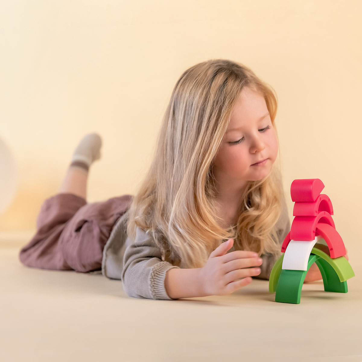 Una niña rubia yace boca abajo jugando con bloques apilables de colores.