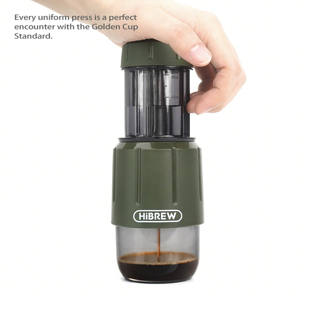 Una mano presiona un extractor de café verde con café en el recipiente inferior.