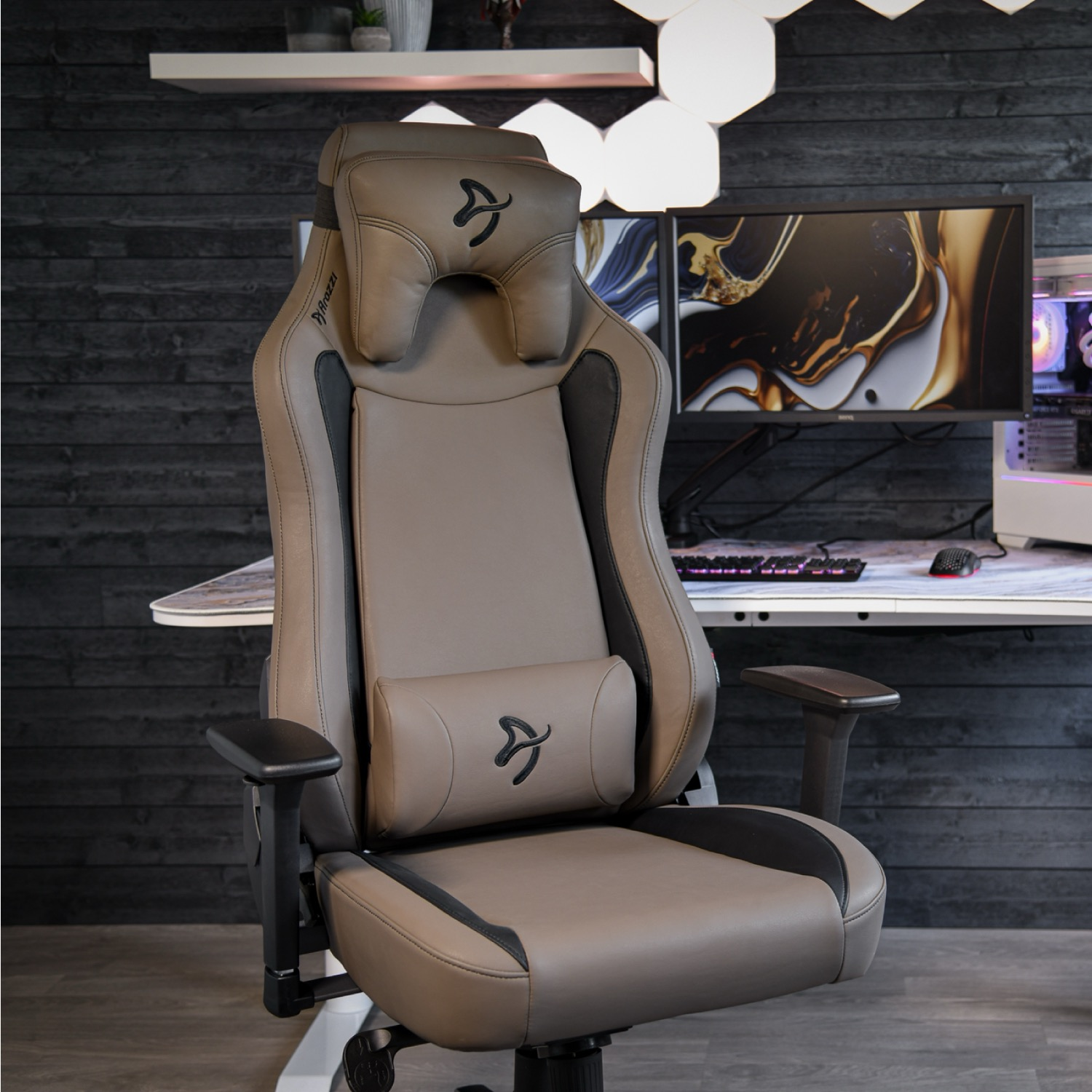 Een beige gamestoel voor een bureau met dubbele monitoren en een pc.