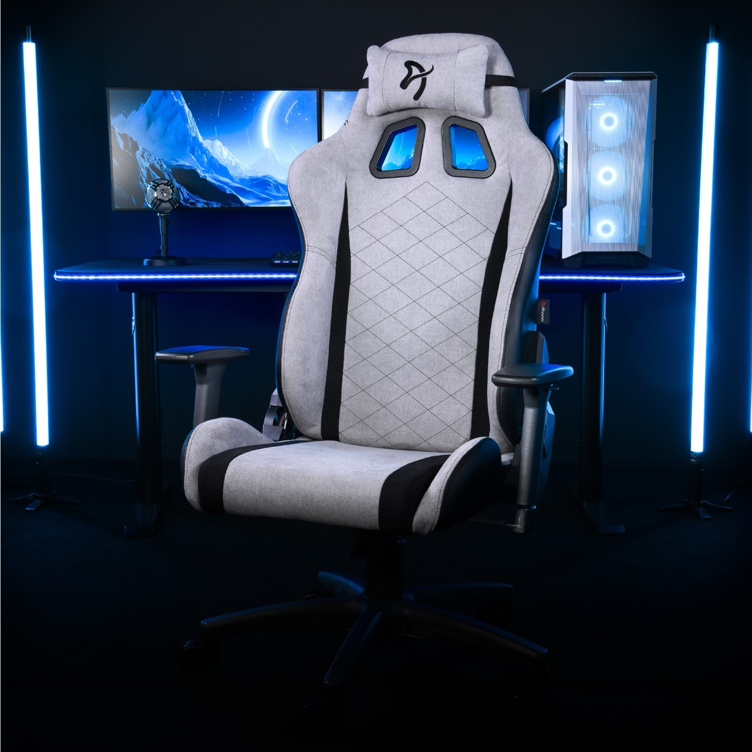Een grijze gamestoel staat voor een bureau met computers en blauwe lichten.