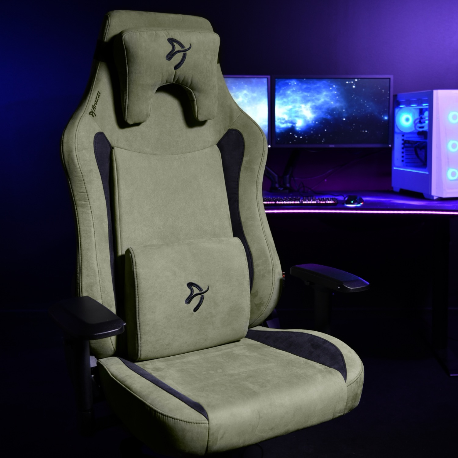 Khakikleurige gamestoel met zwart logo en lendenkussen, voor een bureau met computers.