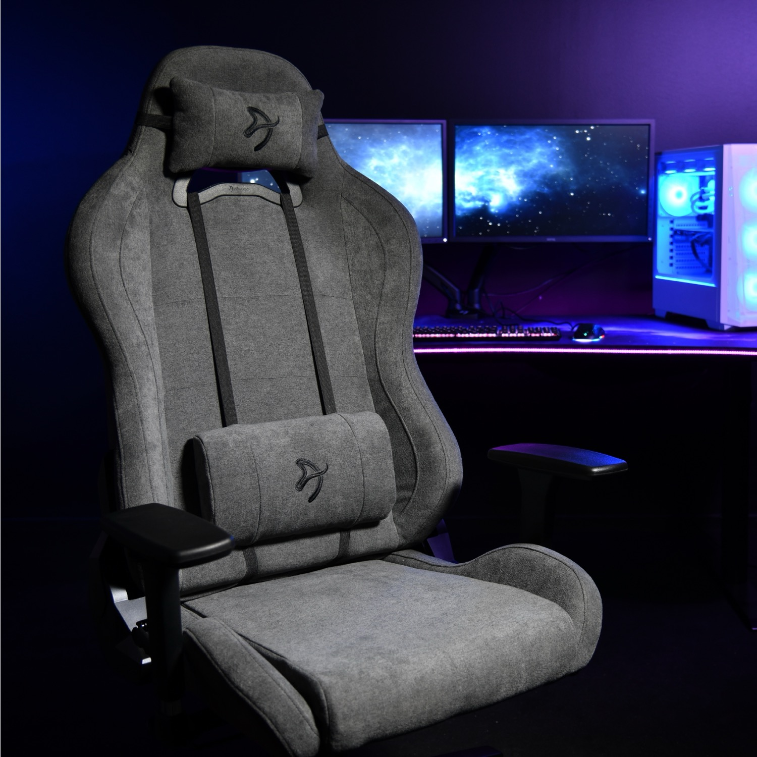 Grijze gamestoel met kussens voor twee monitoren en een pc.