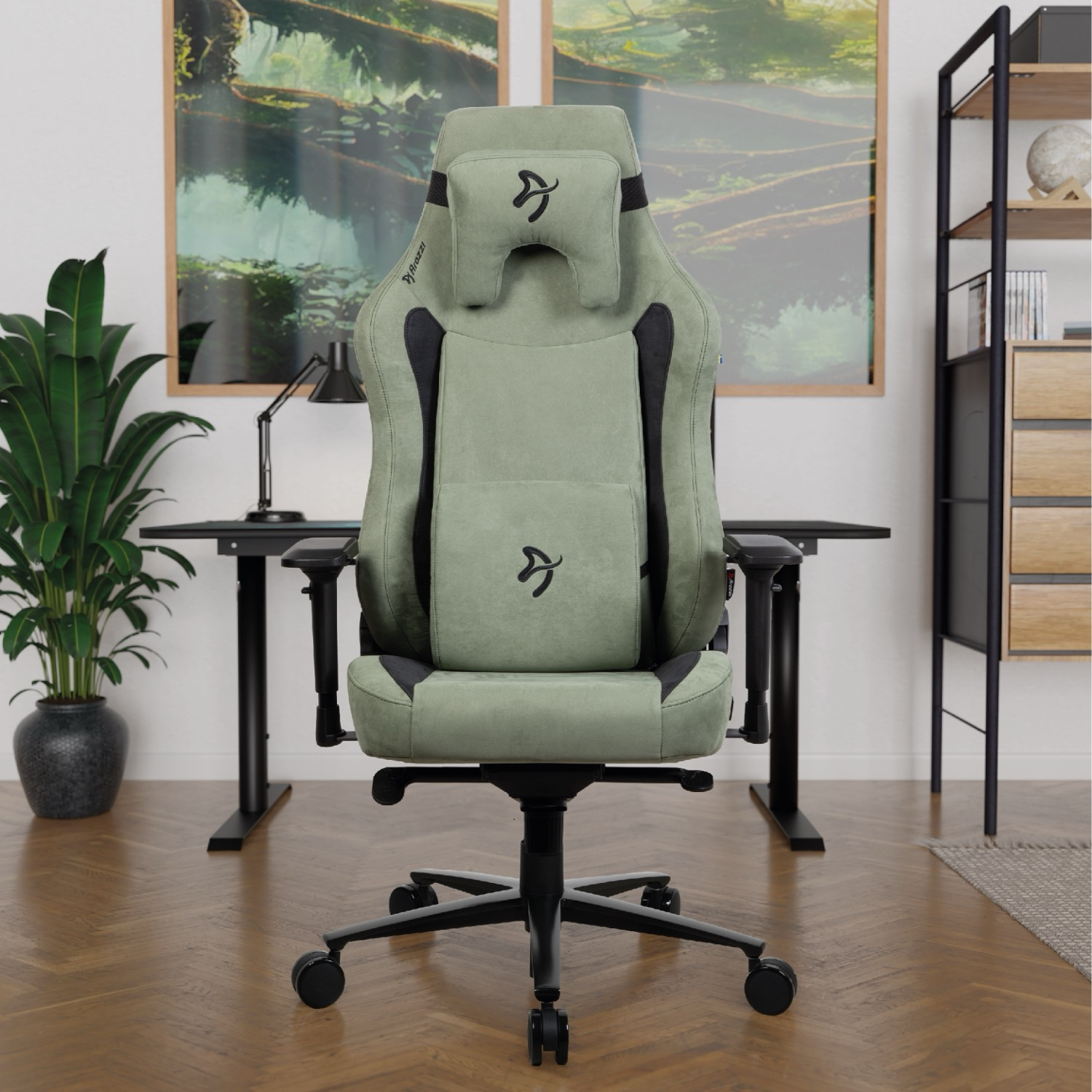 Een groene gamestoel staat op een houten vloer, met een bureau en plant in de buurt.