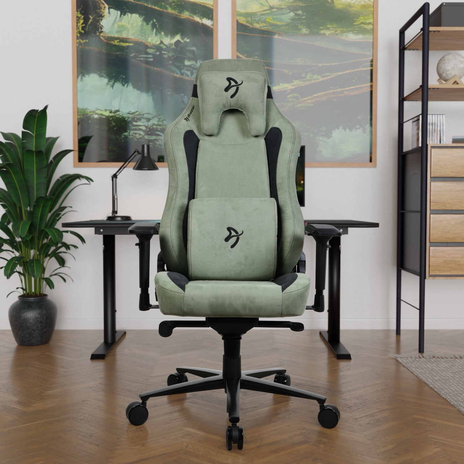 Een groene gamestoel staat voor een bureau met twee schilderijen op de achtergrond.