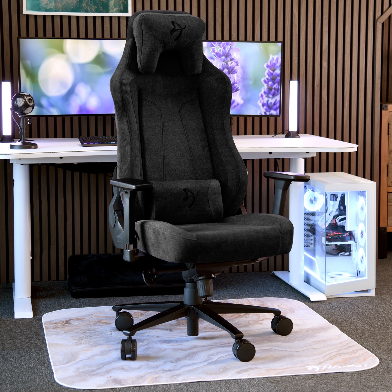 Een zwarte gamestoel staat voor een bureau met een computer en monitors.