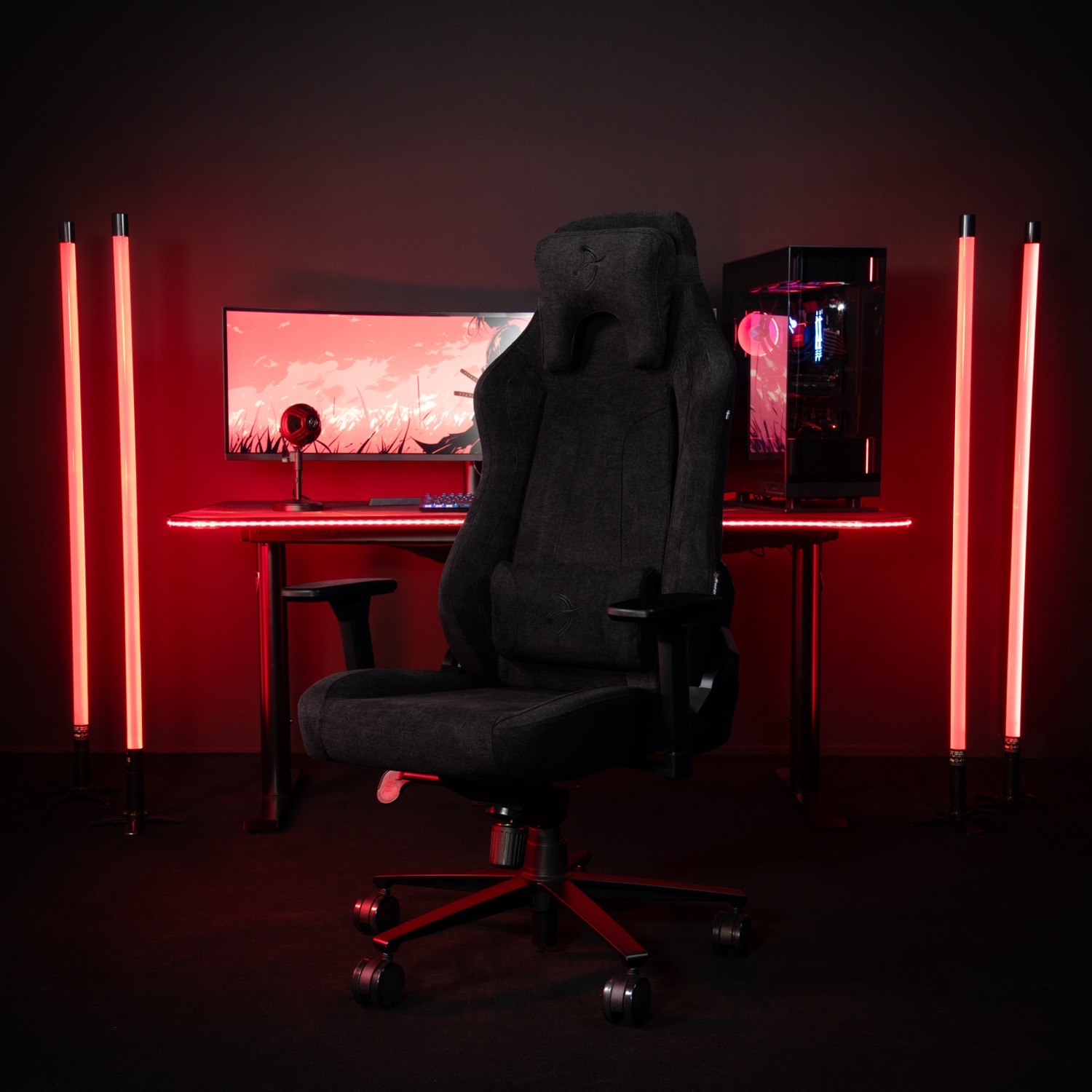 Donkere gamestoel met rode lichten, computer en monitor op een bureau.
