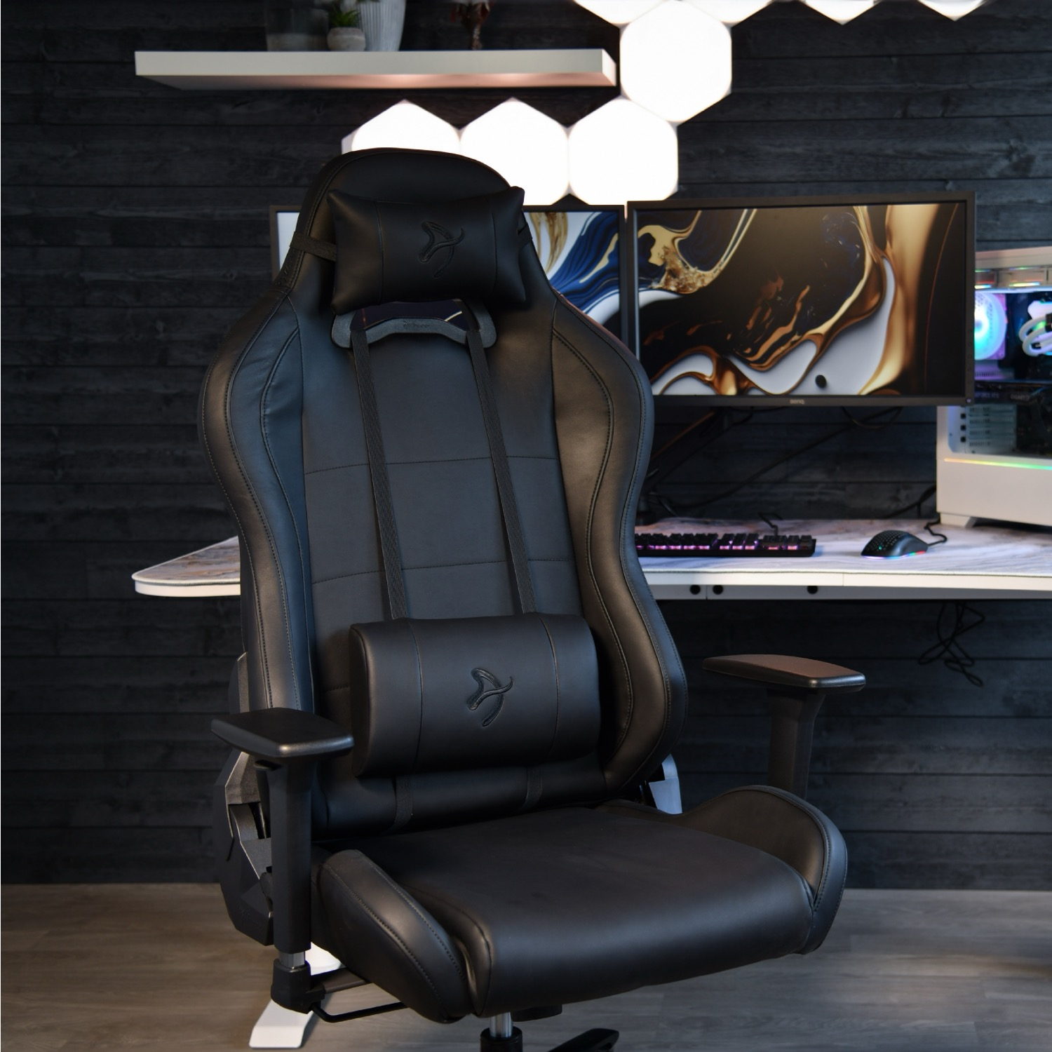 Zwarte gamestoel voor een bureau met monitoren en toetsenbord.
