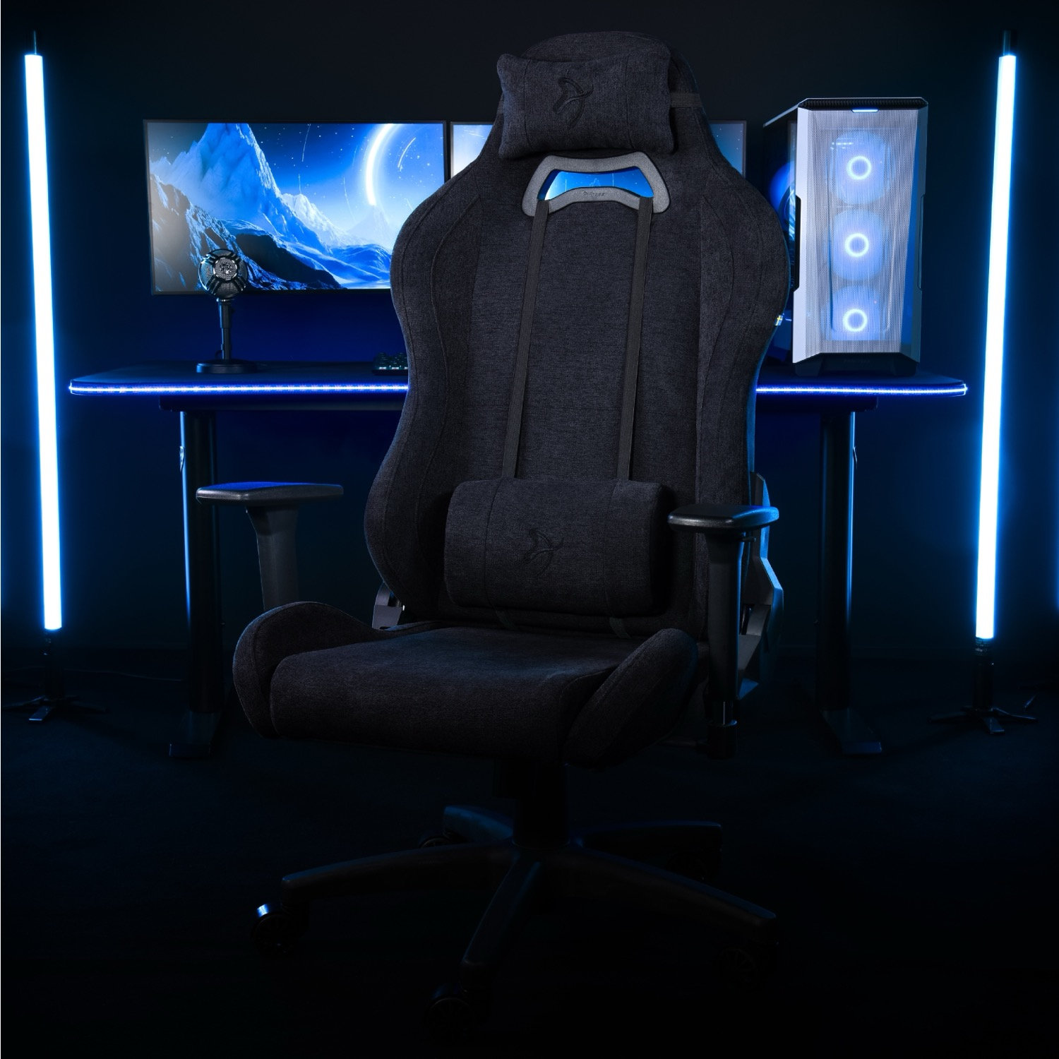 Een donkere gamestoel staat voor een bureau met twee monitoren en een pc.