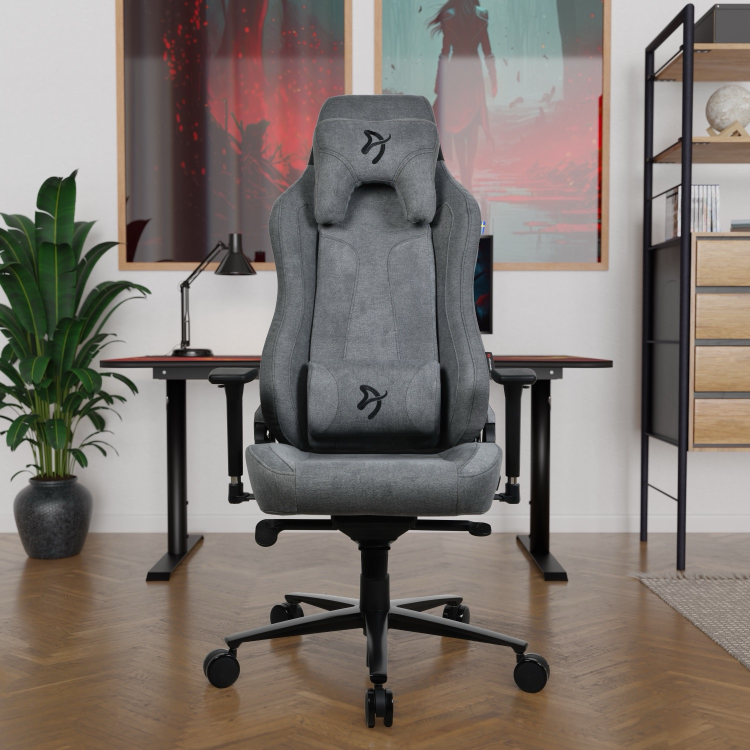 Grijze gamestoel voor een bureau met kunst en een boekenplank.