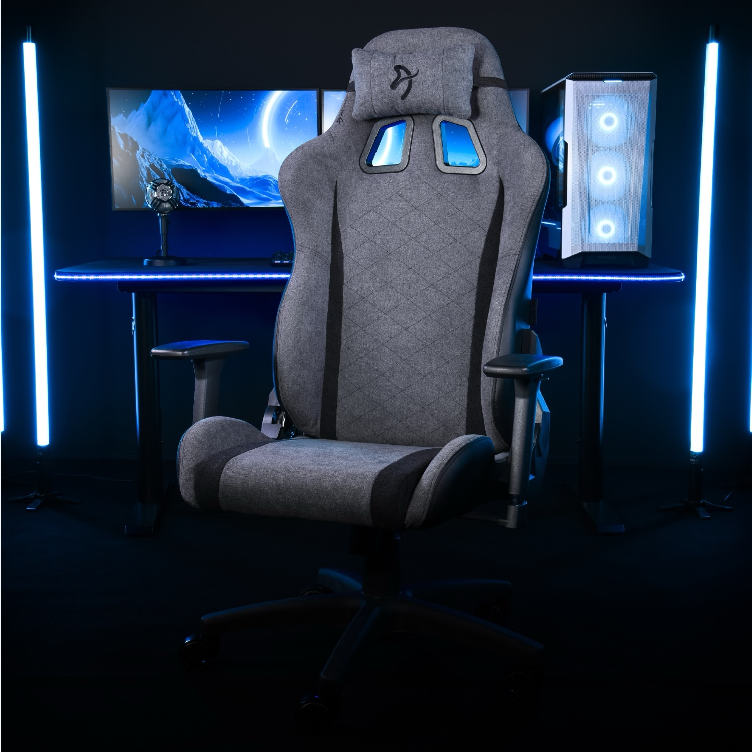 Een grijze gamestoel voor een bureau met twee monitoren en een pc.
