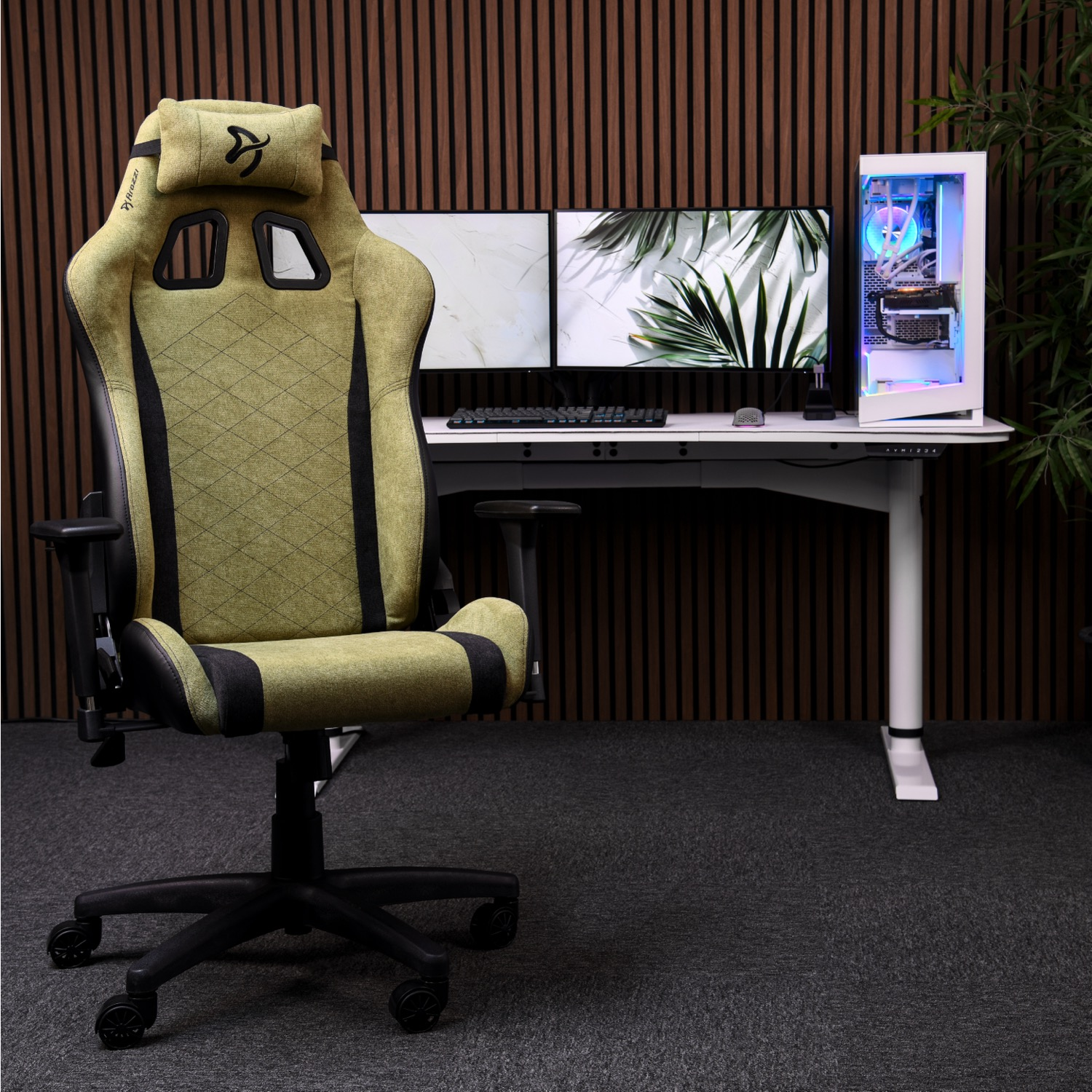 Een groene gamestoel voor een bureau met dubbele monitor, pc en plant.