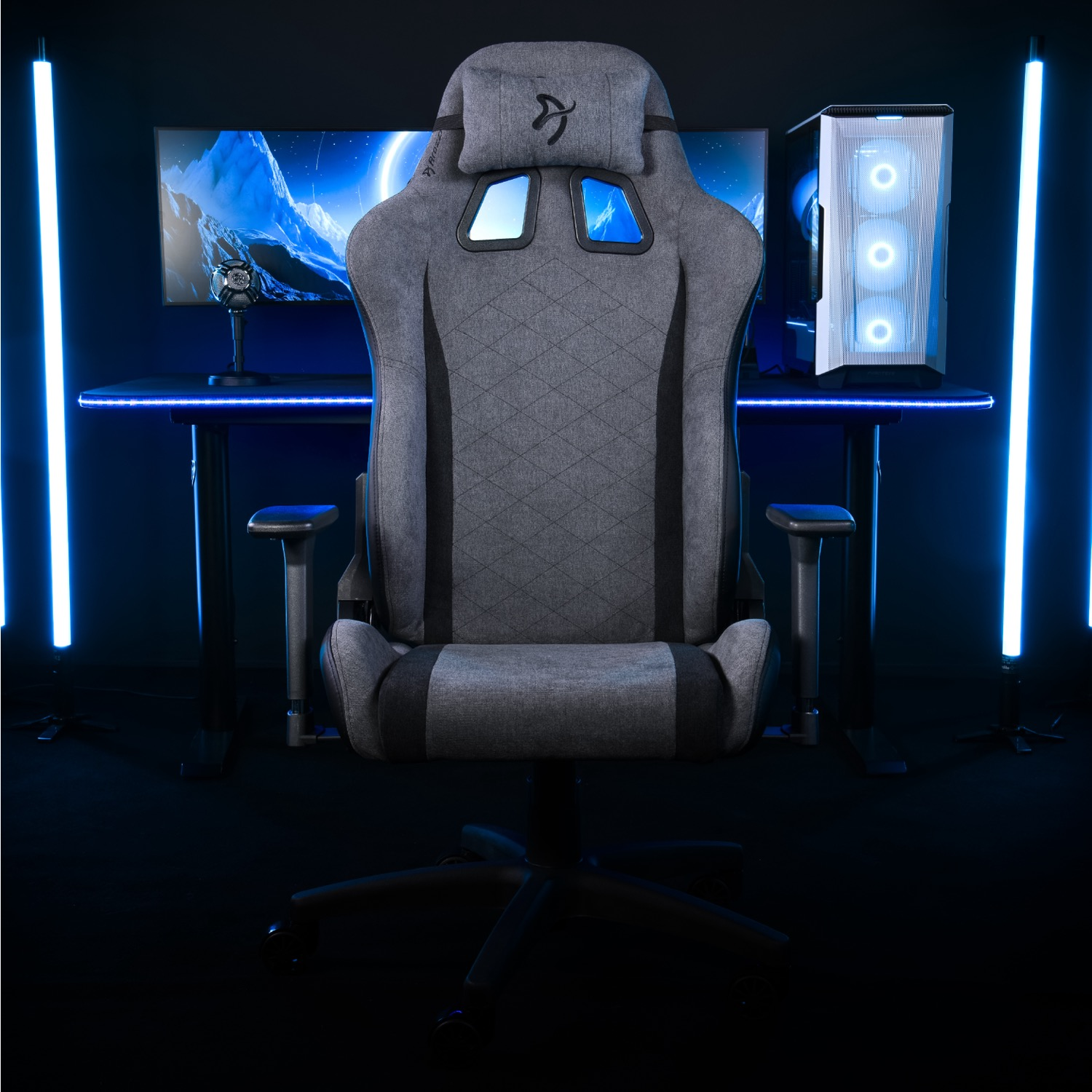 Een grijze gamestoel voor een bureau met computer en monitor. Blauwe lichten gloeien.