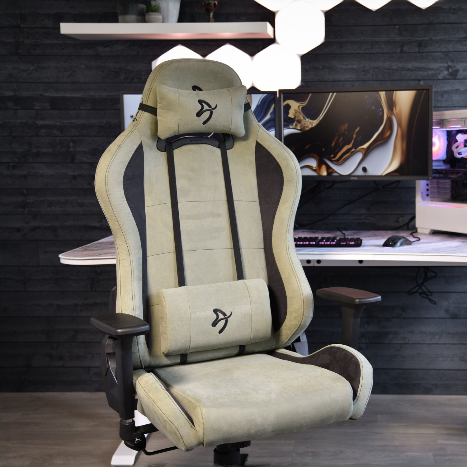 Een beige gamestoel met nek- en lendekussens staat voor een bureau.