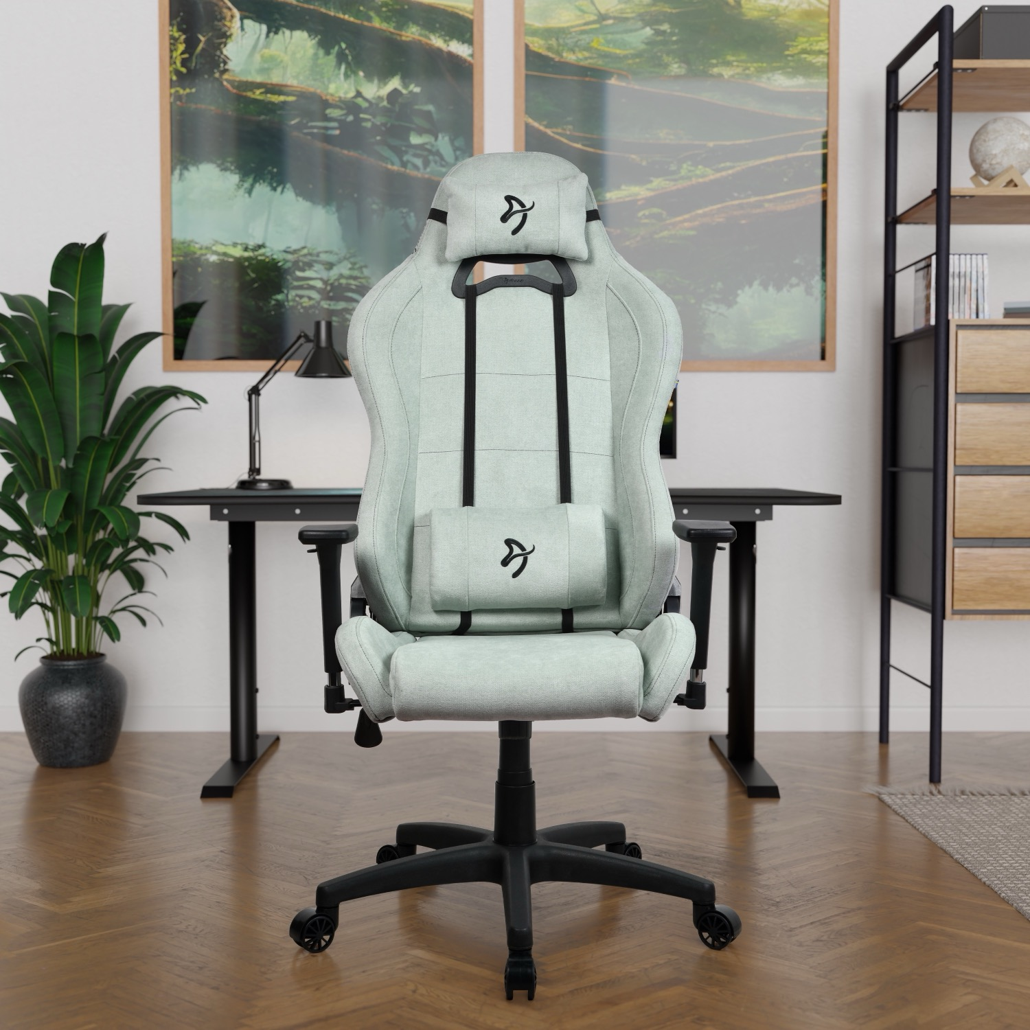 Een lichtgroene gamestoel voor een bureau met twee schilderijen op de achtergrond.