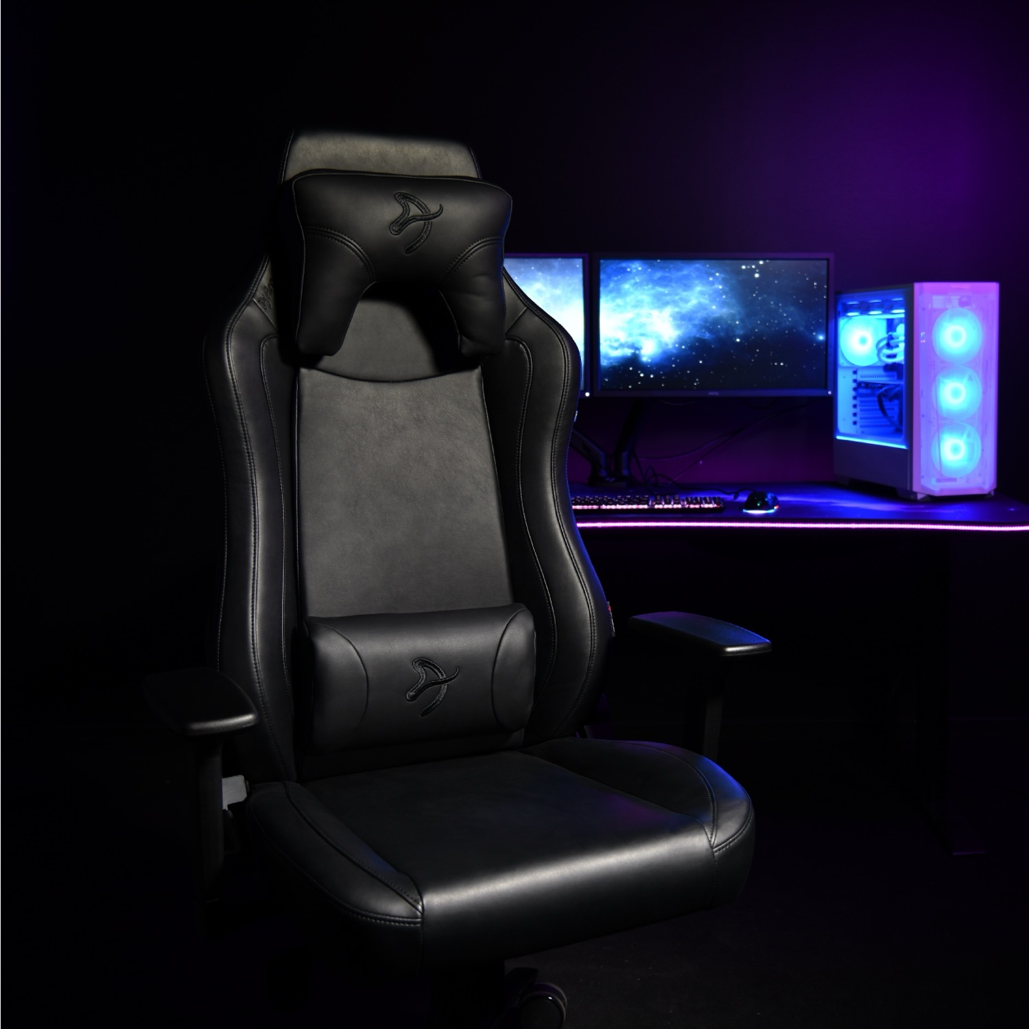 Zwarte gamestoel voor een bureau met twee monitoren en een pc.