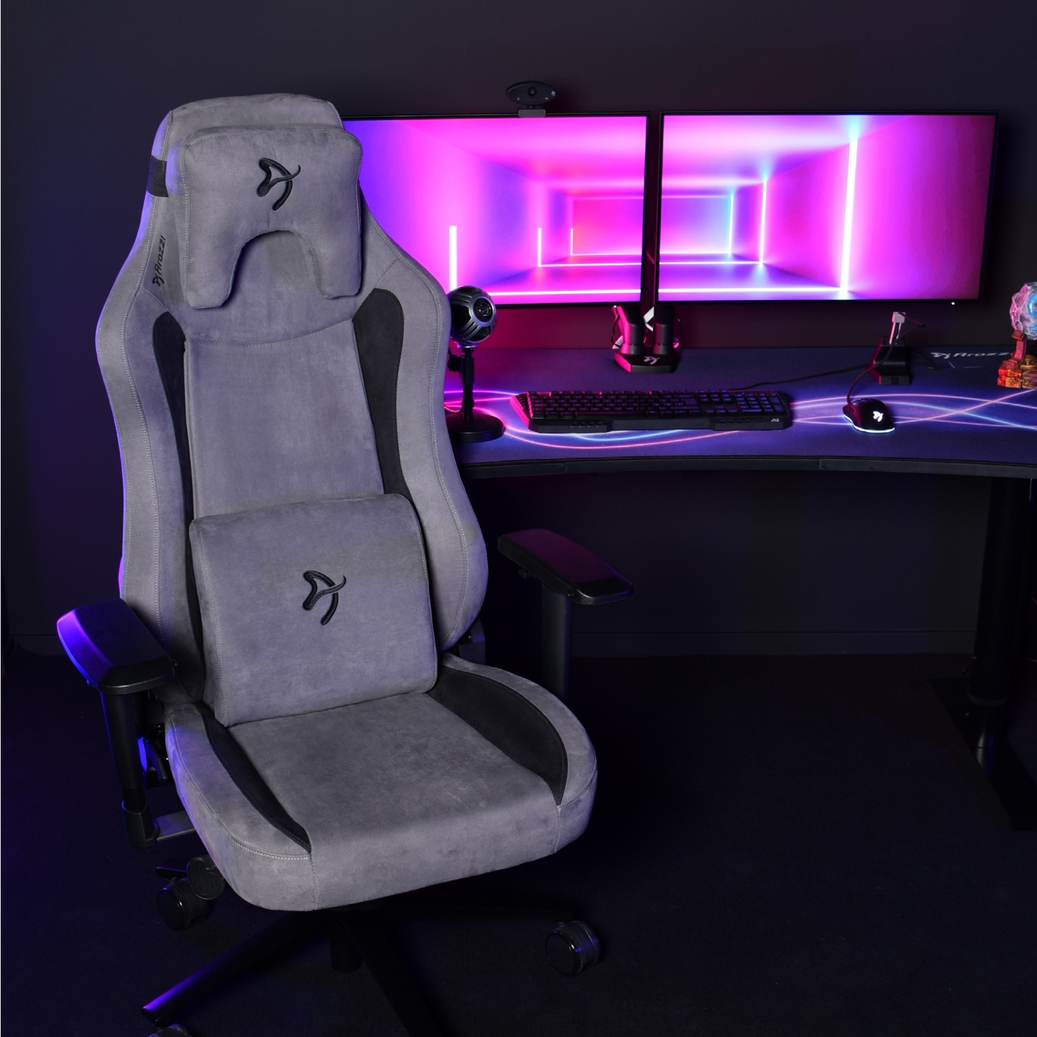 Grijze gamestoel voor een bureau met dubbele monitor, toetsenbord en muis.