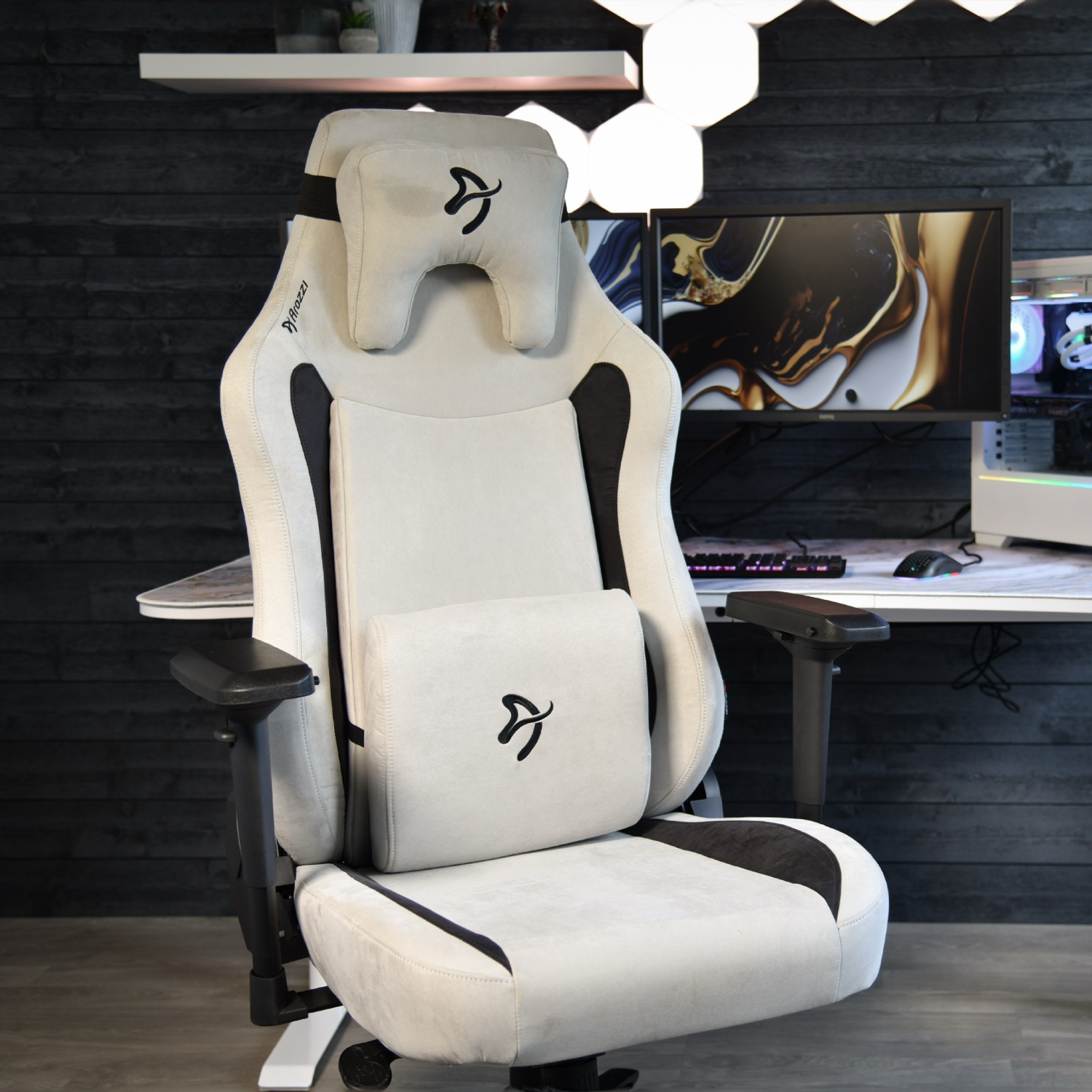 Ein heller Gaming-Stuhl mit schwarzen Akzenten und Kissen steht vor einem Schreibtisch.
