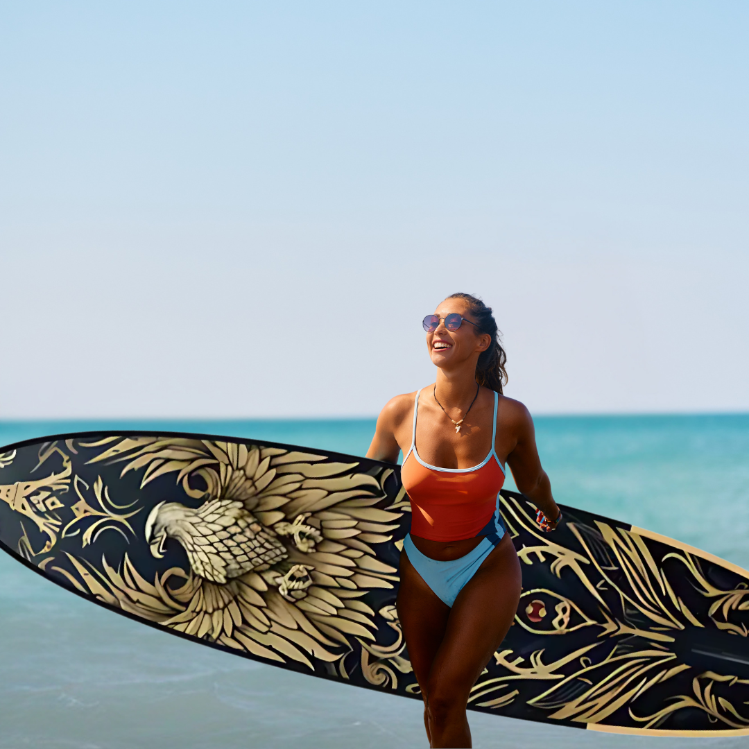 Een vrouw in badkleding draagt een surfboard met adelaarsdesign op het strand.