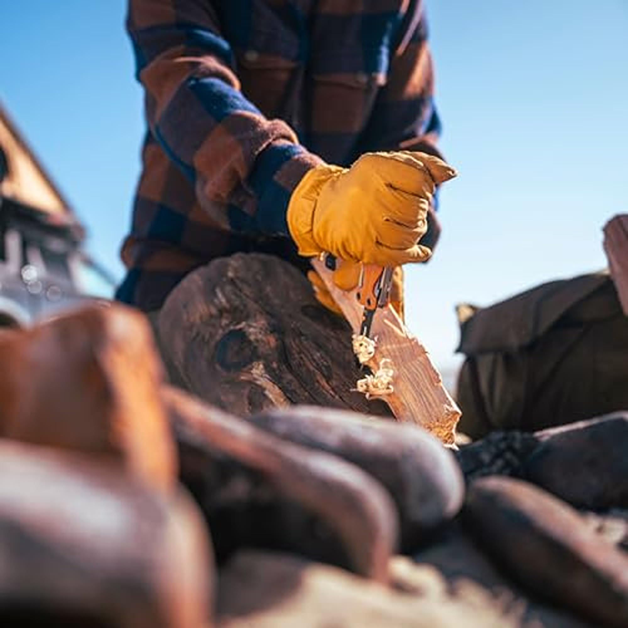 Person schnitzt mit Messer Holz, trägt gelbe Handschuhe und kariertes Hemd.