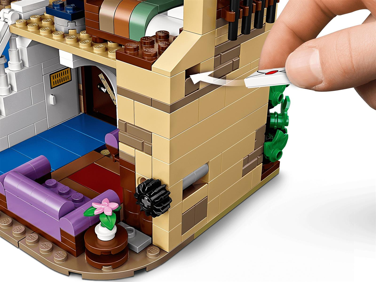 Eine Hand fügt ein weißes Objekt in eine braune Lego-Wand ein. Ein Sofa ist sichtbar.