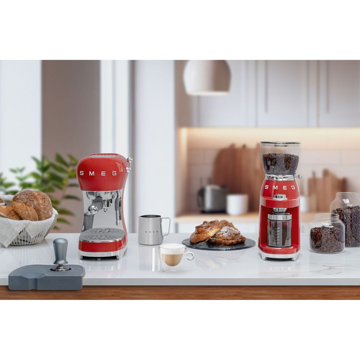 Máquina de espresso y molinillo Smeg rojos sobre encimera con granos de café, pan y pasteles.