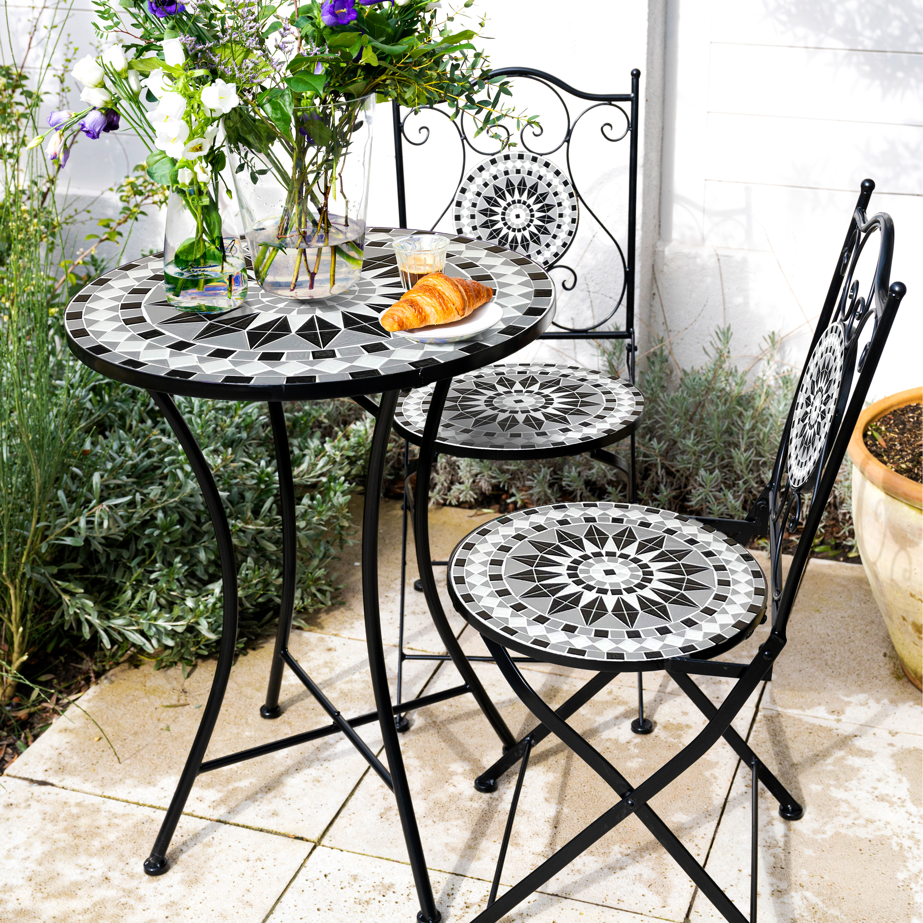 Ein Mosaiktisch und Stühle im Freien mit Blumen und einem Croissant.