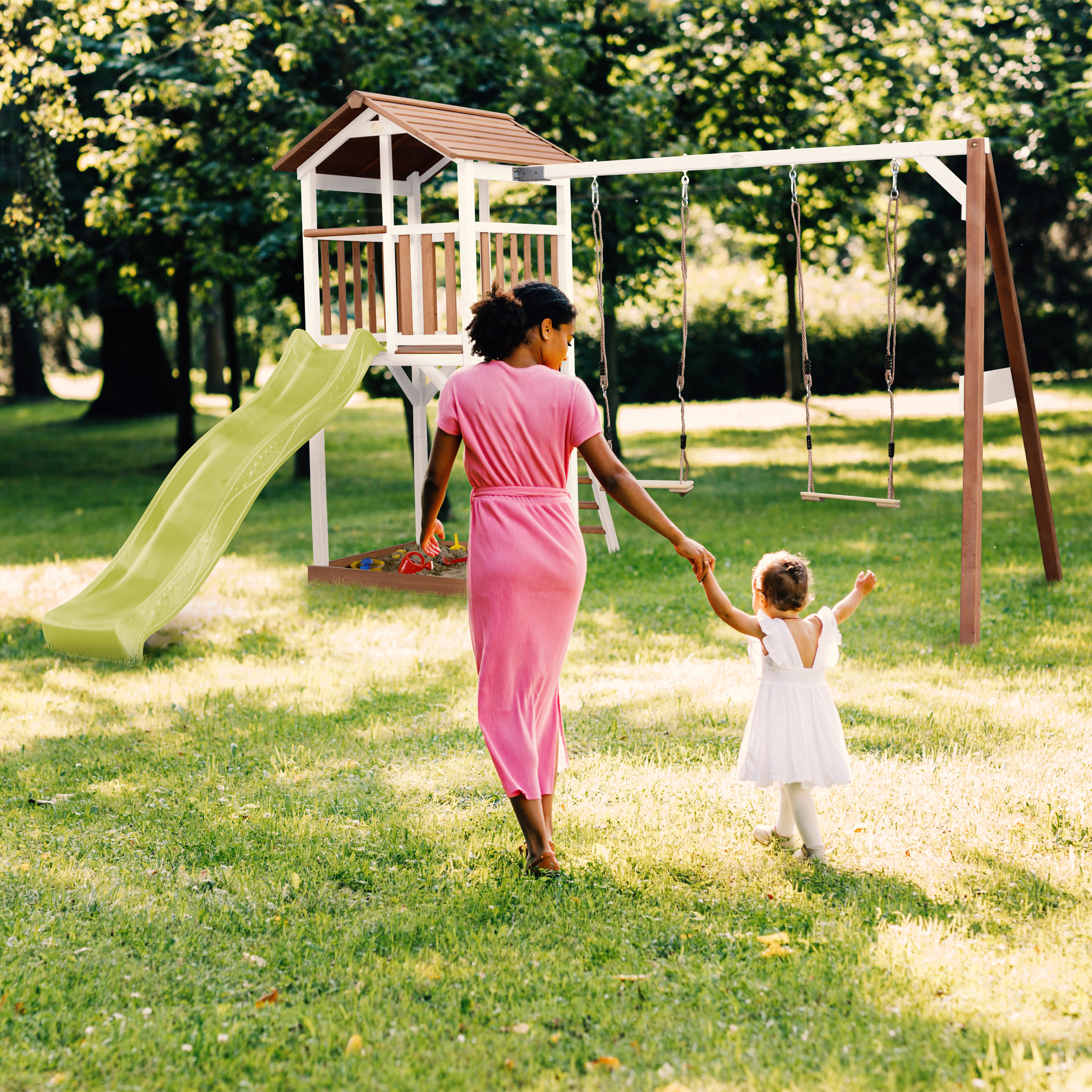 Frau und Kind gehen zum Spielplatz mit Rutsche und Schaukel im Garten.
