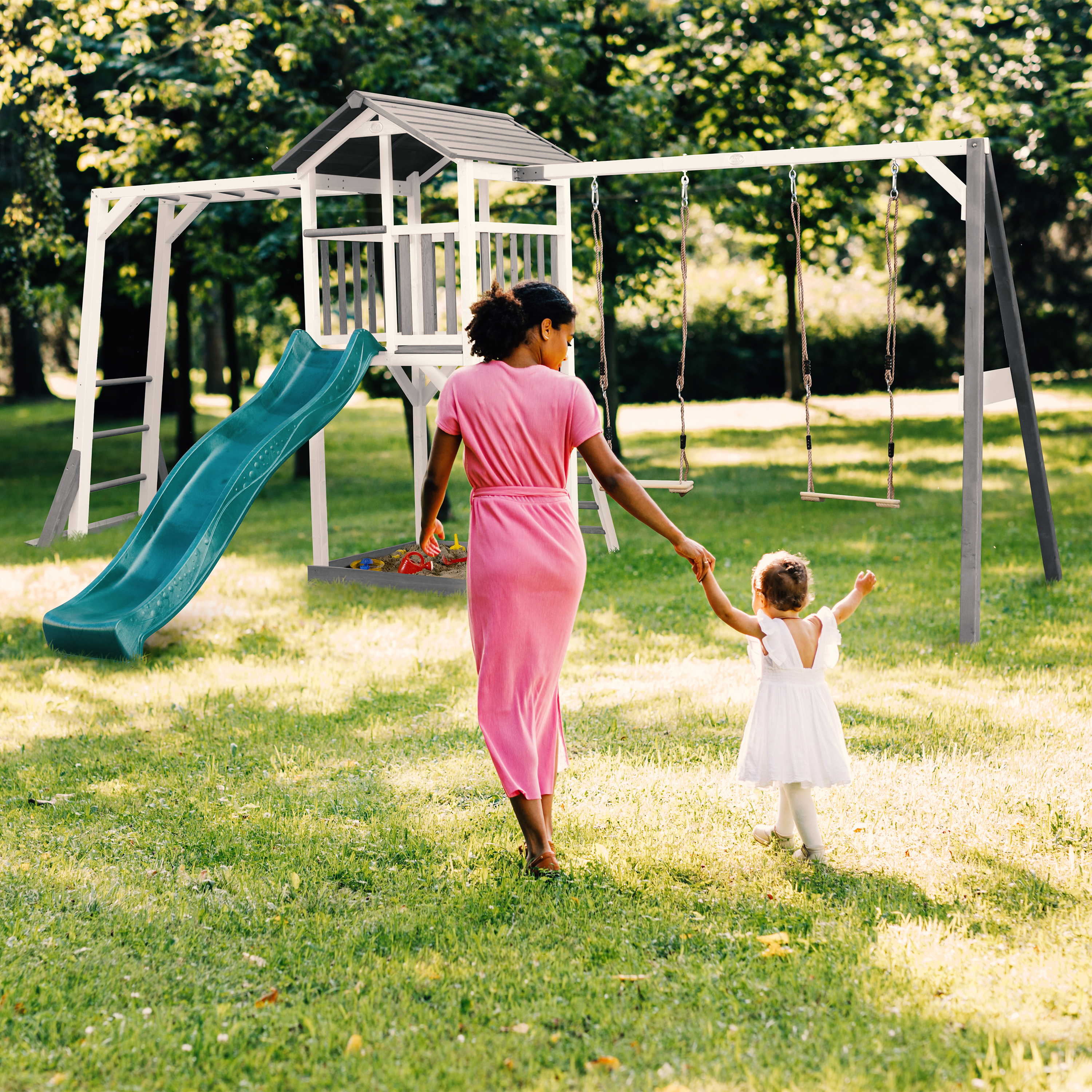 Mutter und Kind gehen zum Spielplatz mit Rutsche und Schaukeln im Garten.