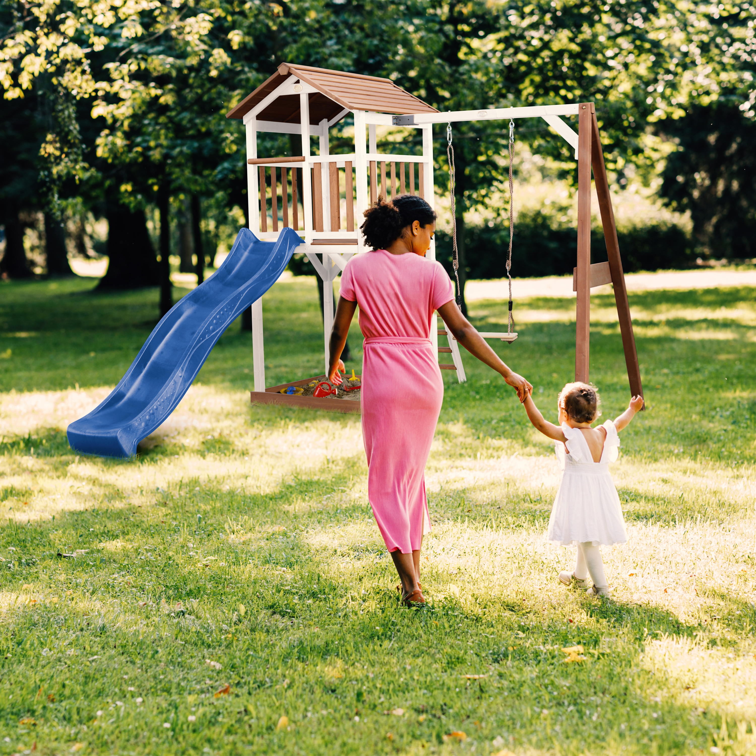 Frau und Kind auf einem Spielplatz mit Rutsche und Schaukel im Freien.